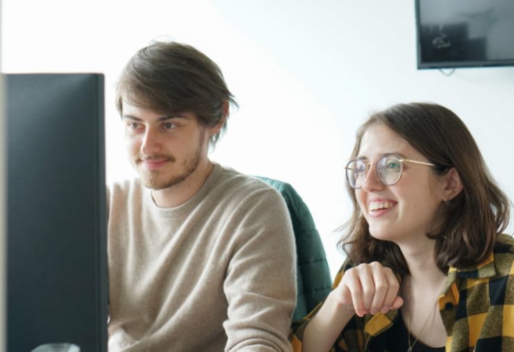 a young man and woman smiling at monitor together