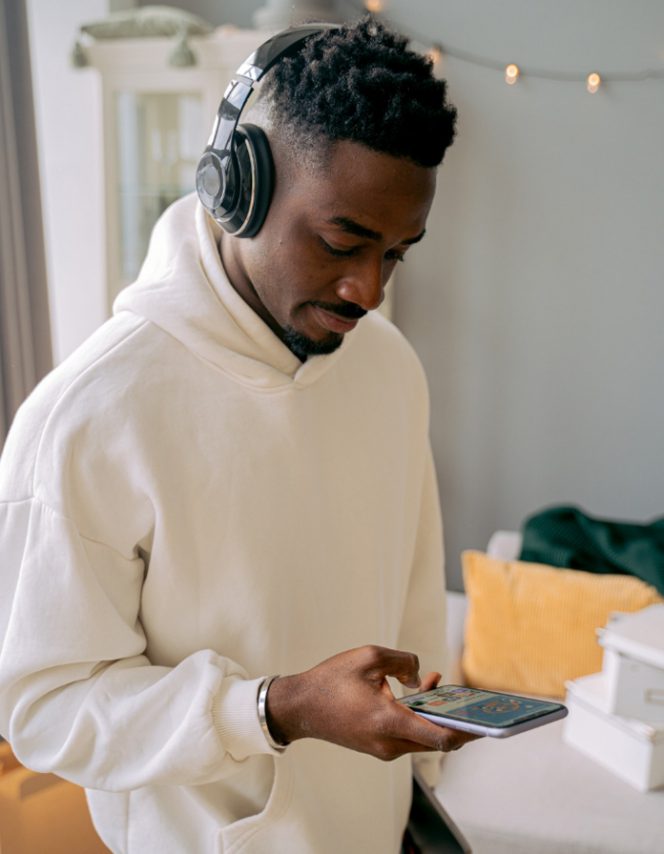 image of young man looking down at his phone with headphones on