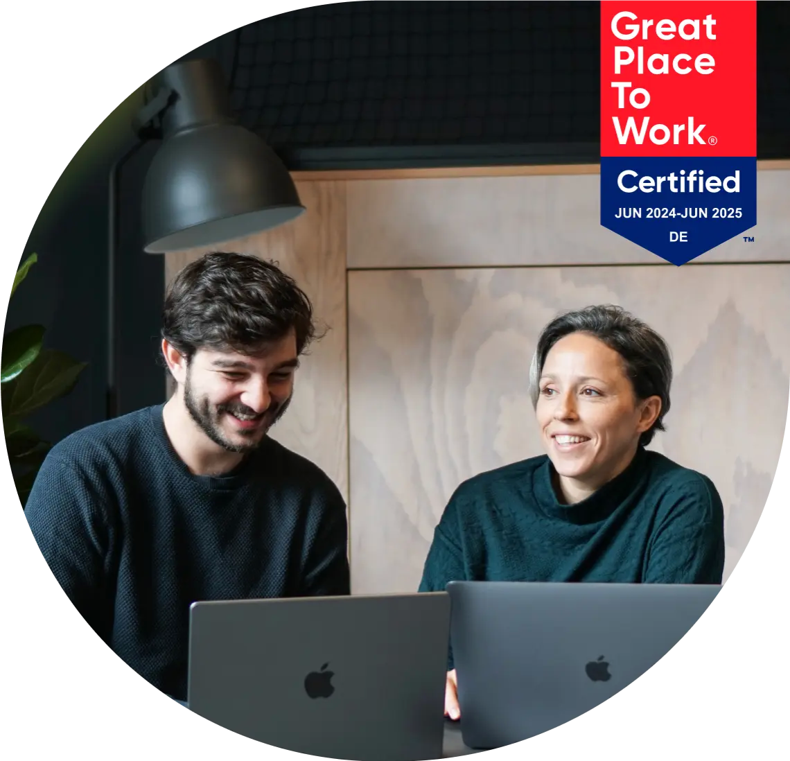 midshot of two young employees at adjoe smiling and working at their laptops